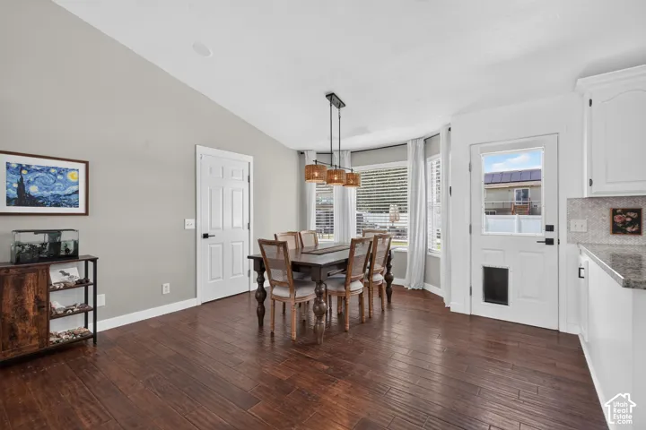 Spacious dining area featuring dark wood-finish flooring, a contemporary linear chandelier, and a bay window with horizontal blinds