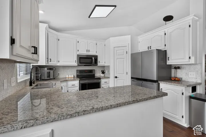 Kitchen featuring white cabinetry with black hardware, stone countertops, a mosaic tile backsplash, and stainless steel appliances