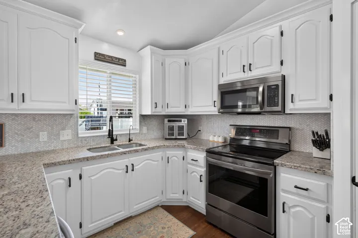 Modern kitchen featuring white cabinetry with black hardware, light-colored speckled countertops, a herringbone pattern backsplash, and stainless steel appliances