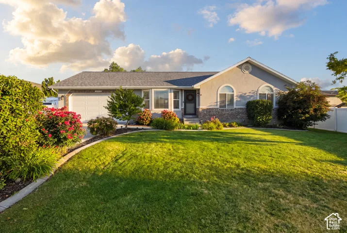 Single-story exterior featuring a stone and stucco facade, arched windows, attached two-car garage, and a manicured front lawn with perimeter landscaping