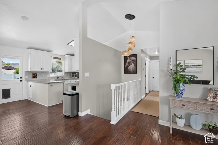Open-concept interior featuring wood-finish flooring, a white kitchen with light-toned countertops and backsplash, white cabinetry, and a white staircase with balusters