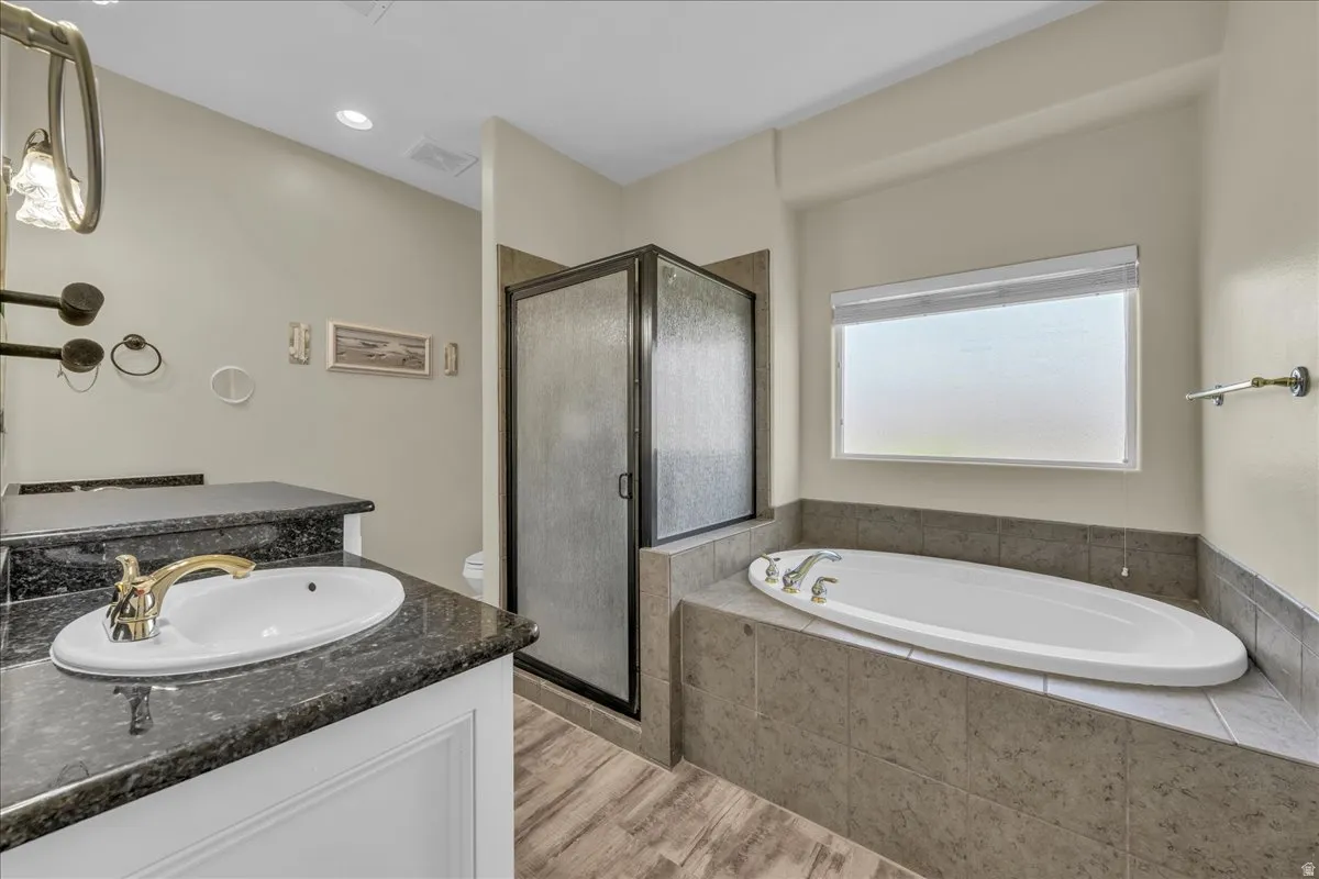 Bathroom featuring a built-in tub, a glass-enclosed shower, a vanity with an undermount sink, and wood-finish flooring