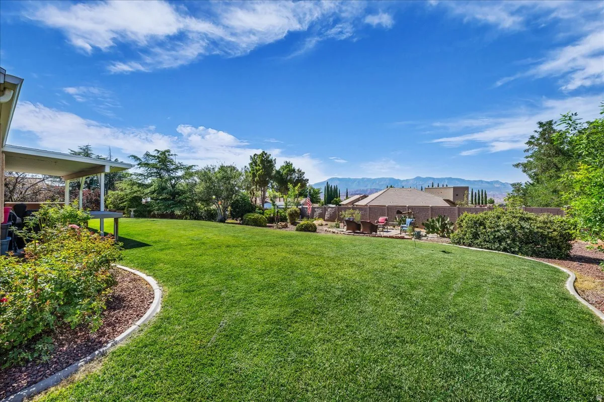 Expansive green lawn with concrete curbing, mature landscaping, and a covered patio structure