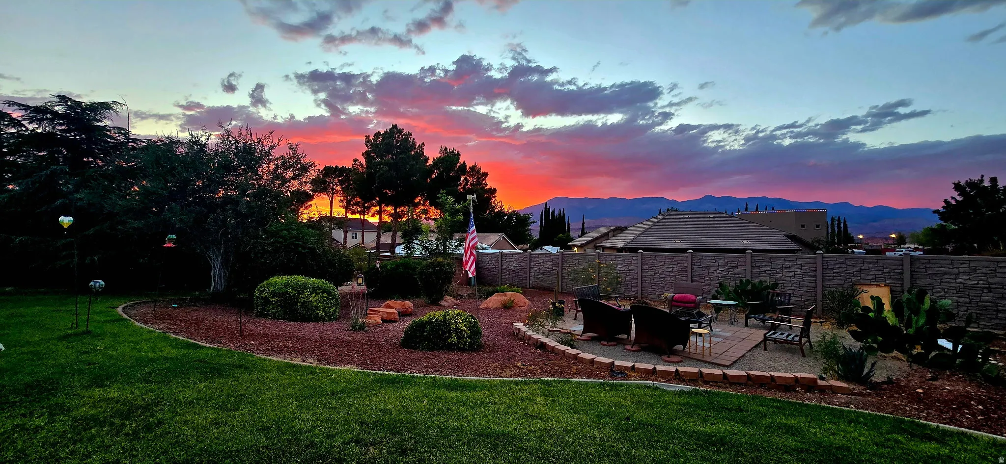Expansive backyard featuring a brick paver patio, lush green lawn, mature landscaping, and a privacy fence