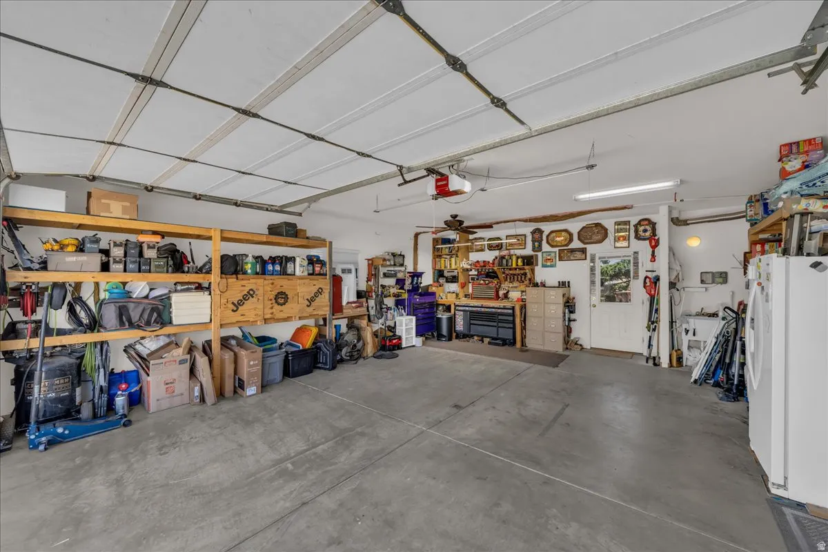 Spacious garage featuring a concrete floor, built-in shelving, a workbench, and a ceiling fan