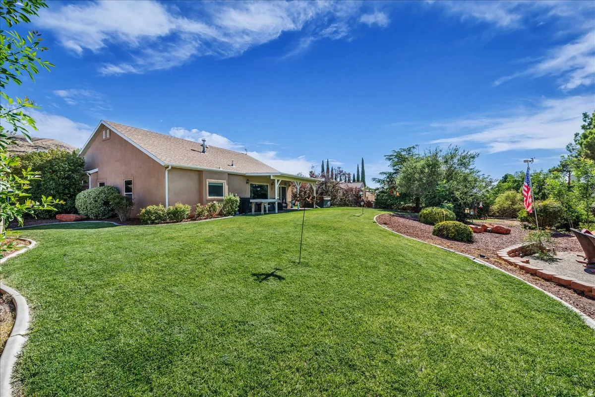 Expansive green lawn with a defined concrete border, complemented by a covered patio area and mature landscaping