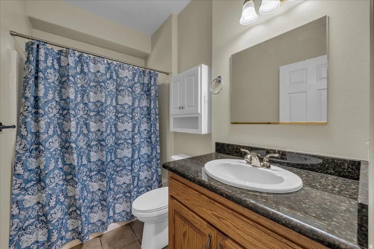 Bathroom featuring a granite-look countertop, undermount sink, wood-finish vanity, and a shower with a curtain rod