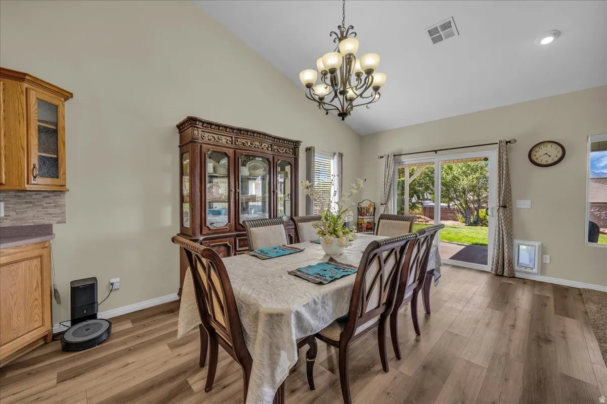Vaulted ceiling dining area featuring wood-finish flooring, a decorative chandelier, and sliding glass doors providing outdoor access
