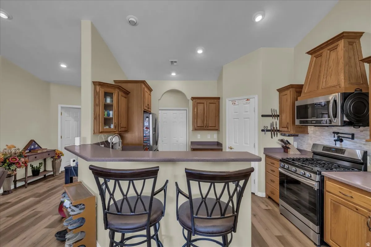 Kitchen featuring wood cabinetry, stainless steel range and microwave, a tile backsplash, and a breakfast bar