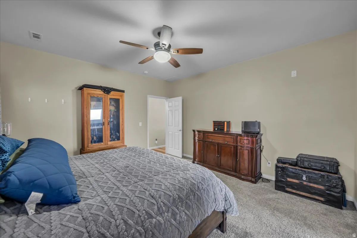 Spacious room featuring neutral wall tones, textured carpet flooring, and a ceiling fan with integrated lighting