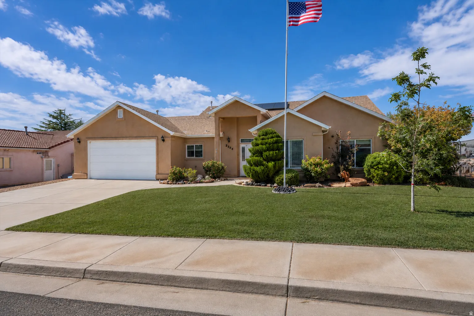 Stucco exterior with an attached garage, paved driveway, and a landscaped front lawn