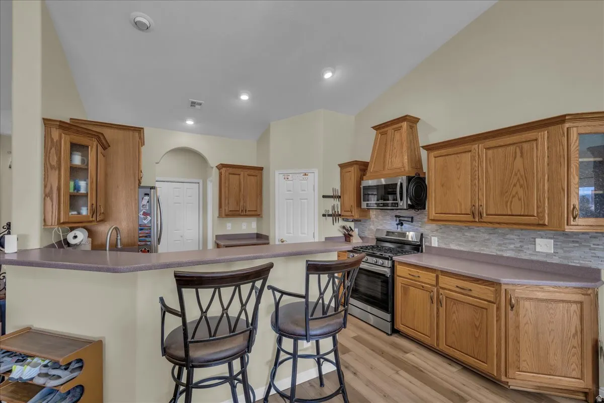 Kitchen featuring wood-finish cabinetry, stainless steel appliances, a light-toned backsplash, a breakfast bar, and wood-finish flooring