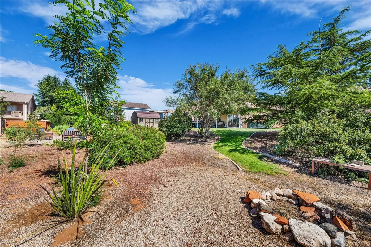 Spacious outdoor area featuring a central fire pit, established trees, and a gravel ground cover