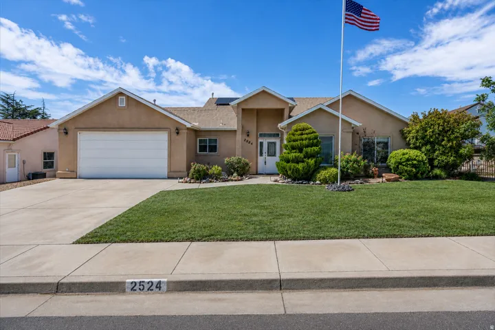 Stucco exterior residence featuring an attached garage, concrete driveway, and a front yard with mature landscaping and green lawn