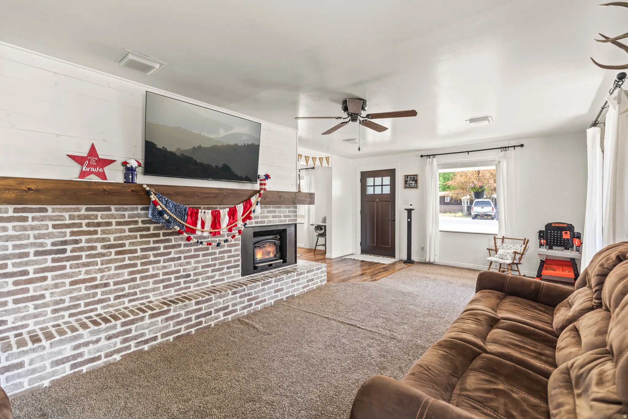 Brick fireplace with a wood mantle, wood-finish flooring, ceiling fan, and front door with glass windowpanes