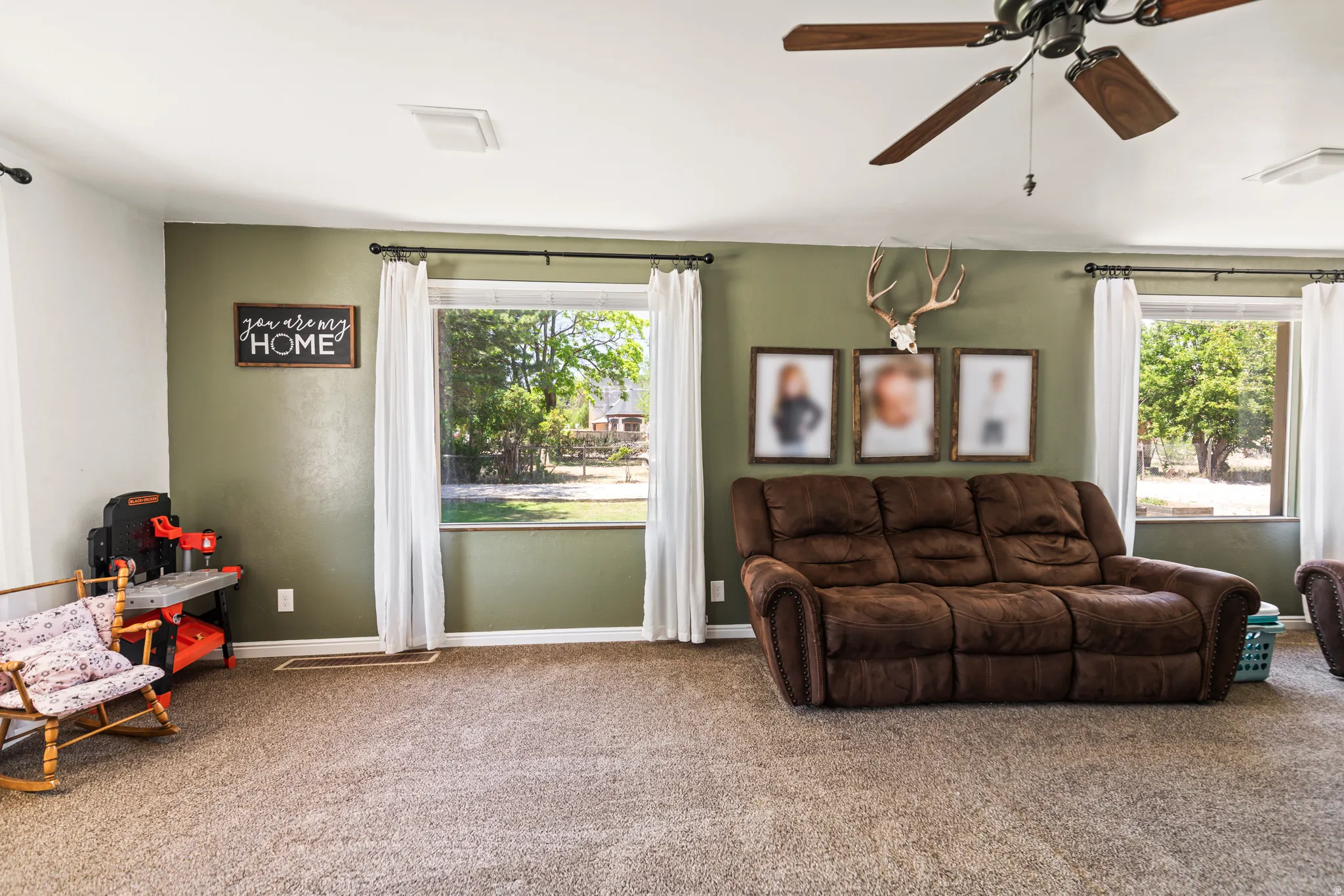 Spacious room featuring broad windows with white drapery and a ceiling fan with wood-finish blades