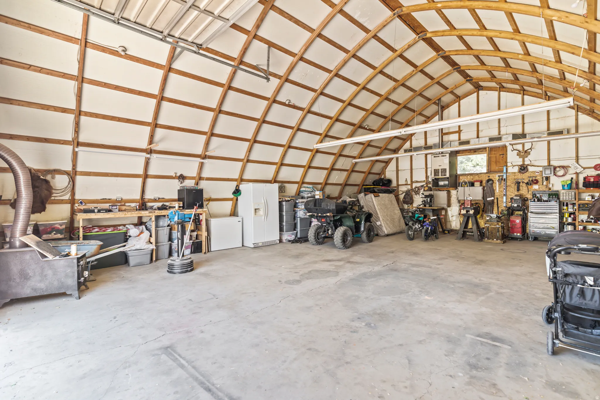 Spacious garage featuring a high arched ceiling with exposed wood framing, concrete flooring, and extensive workspace with built-in shelving