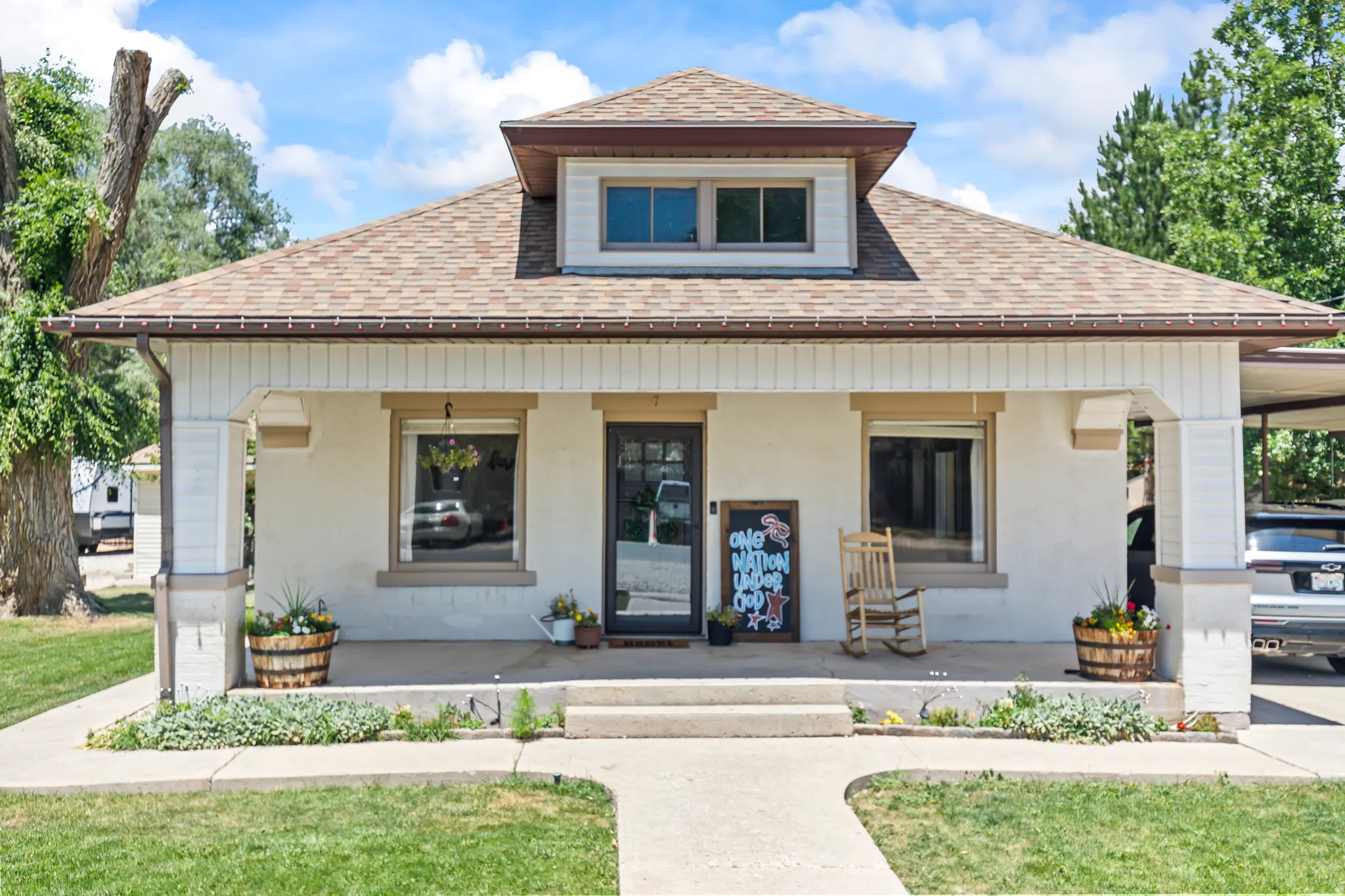 White stucco exterior with a brown shingle roof and dormer window