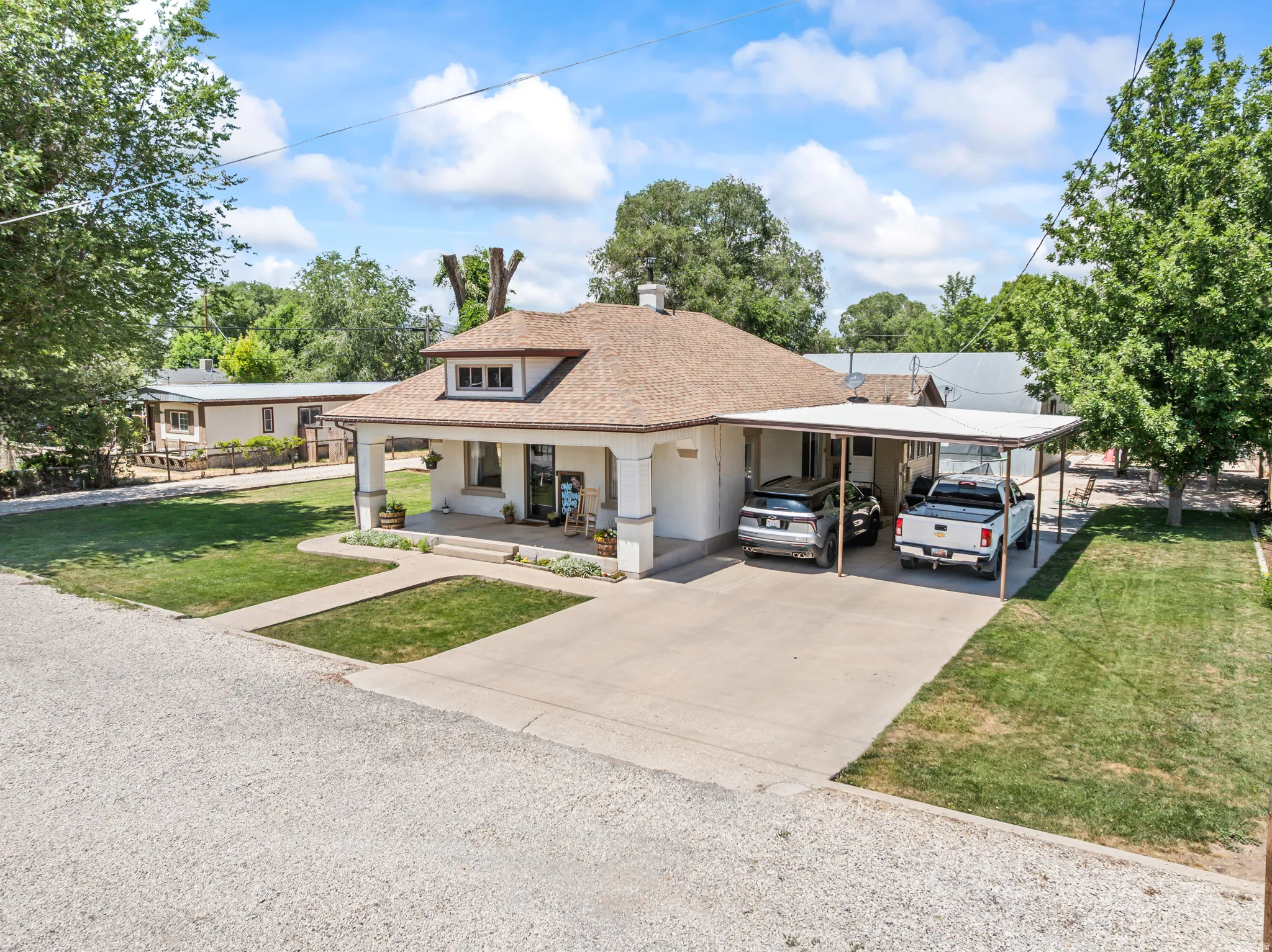 Traditional stucco home with a covered front porch, dormer window, and a concrete driveway leading to a multi-car carport