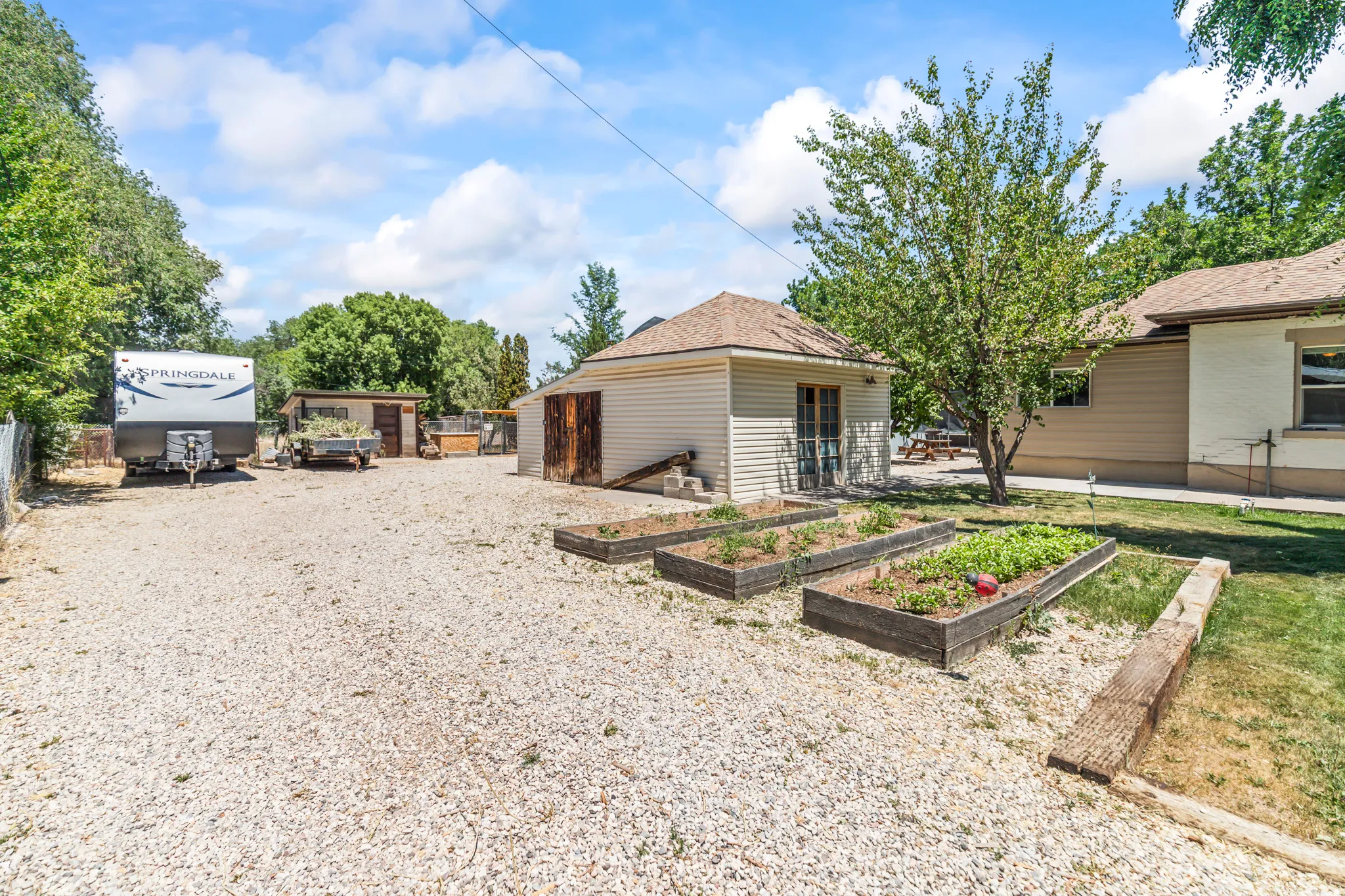 Gravel yard area featuring three raised garden beds, a detached outbuilding with siding, and a fenced perimeter