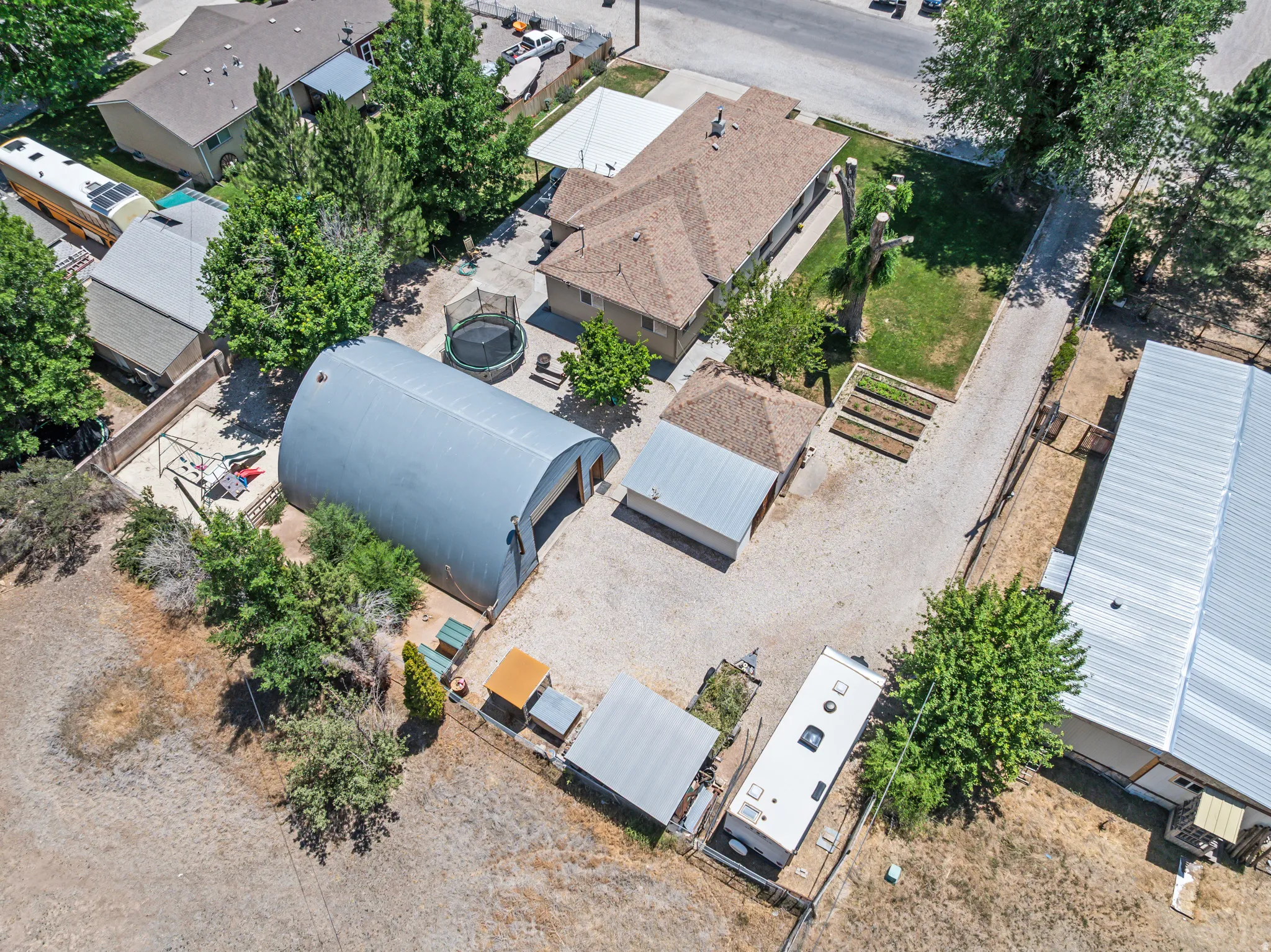 Expansive gravel lot featuring a large quonset hut, covered carport, raised garden beds, and a grass lawn