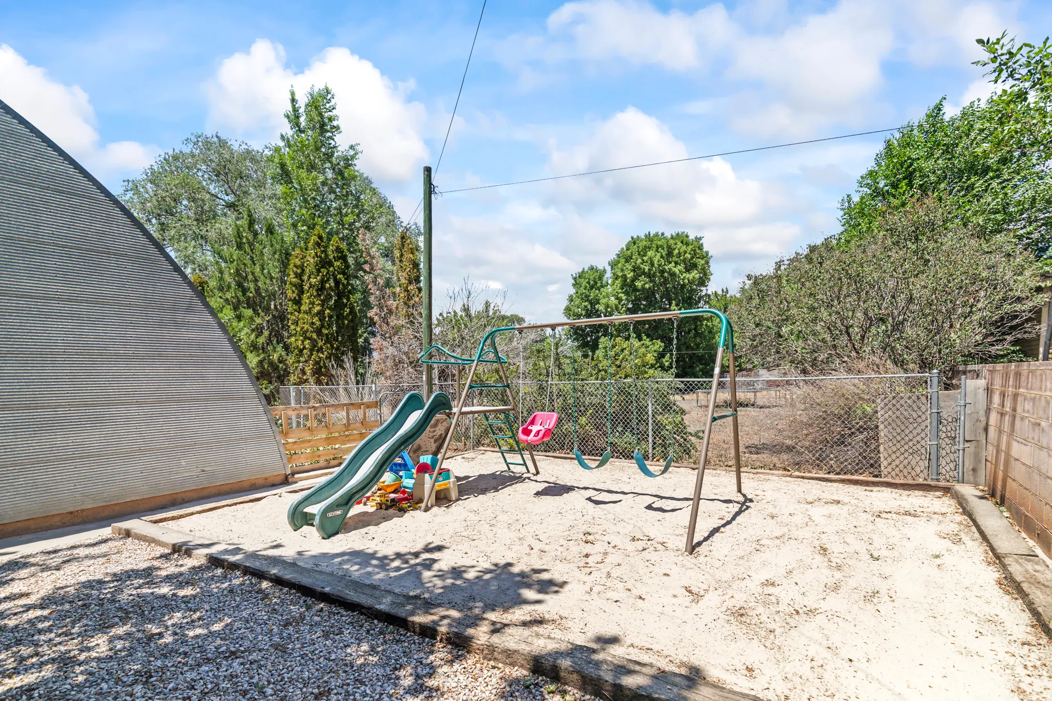Enclosed play area featuring a large sandbox, swing set with slide, and fenced perimeter