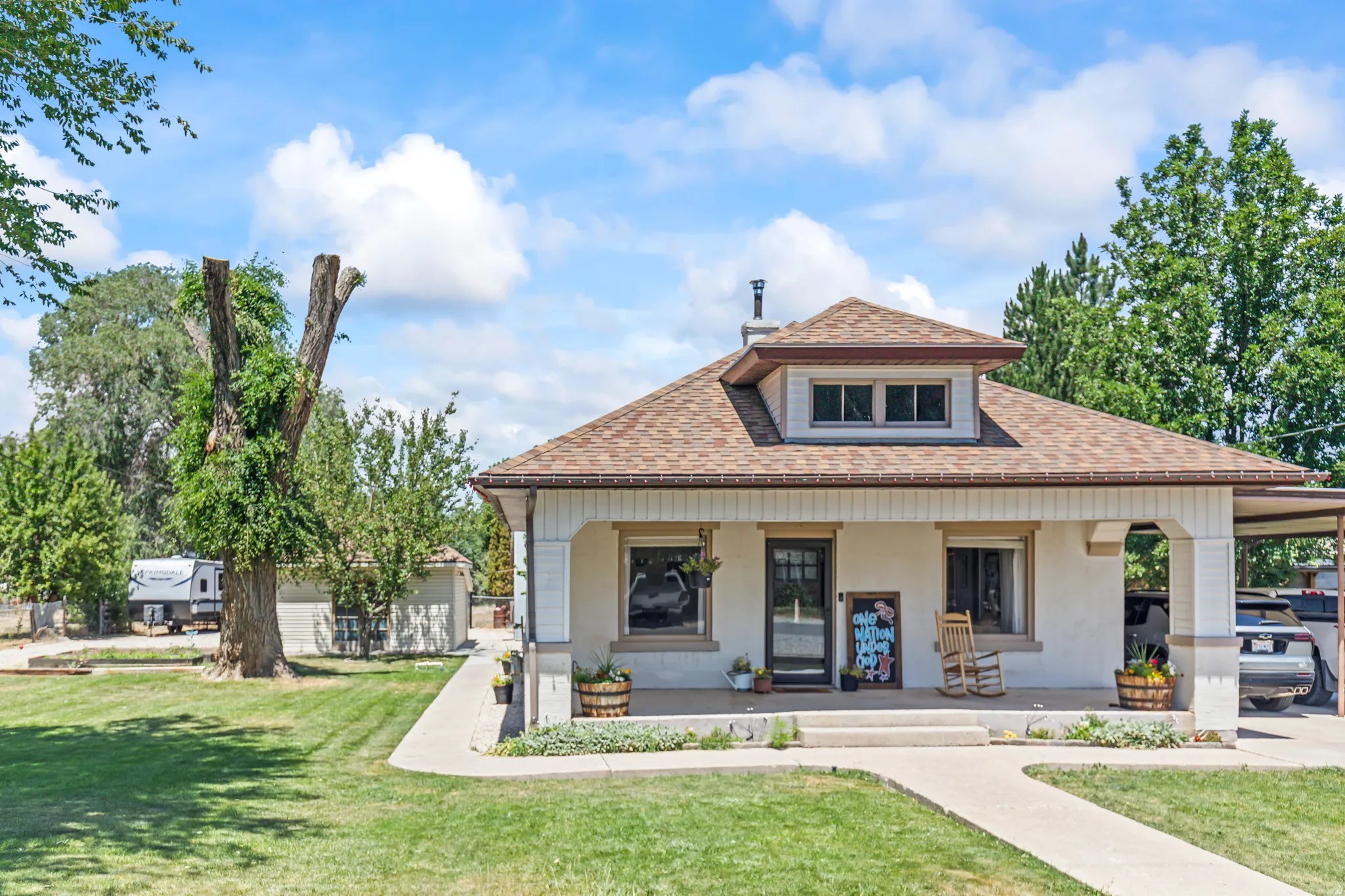 Stucco exterior residence featuring a front porch with white columns, a dormer window, and a carport