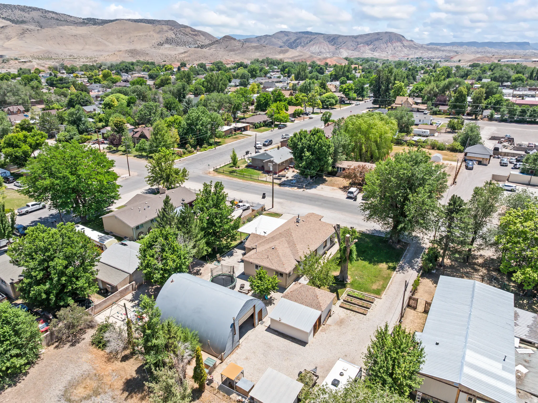 Aerial property perspective featuring a residential structure with a brown shingle roof, a large Quonset hut-style metal building, and a smaller detached shed