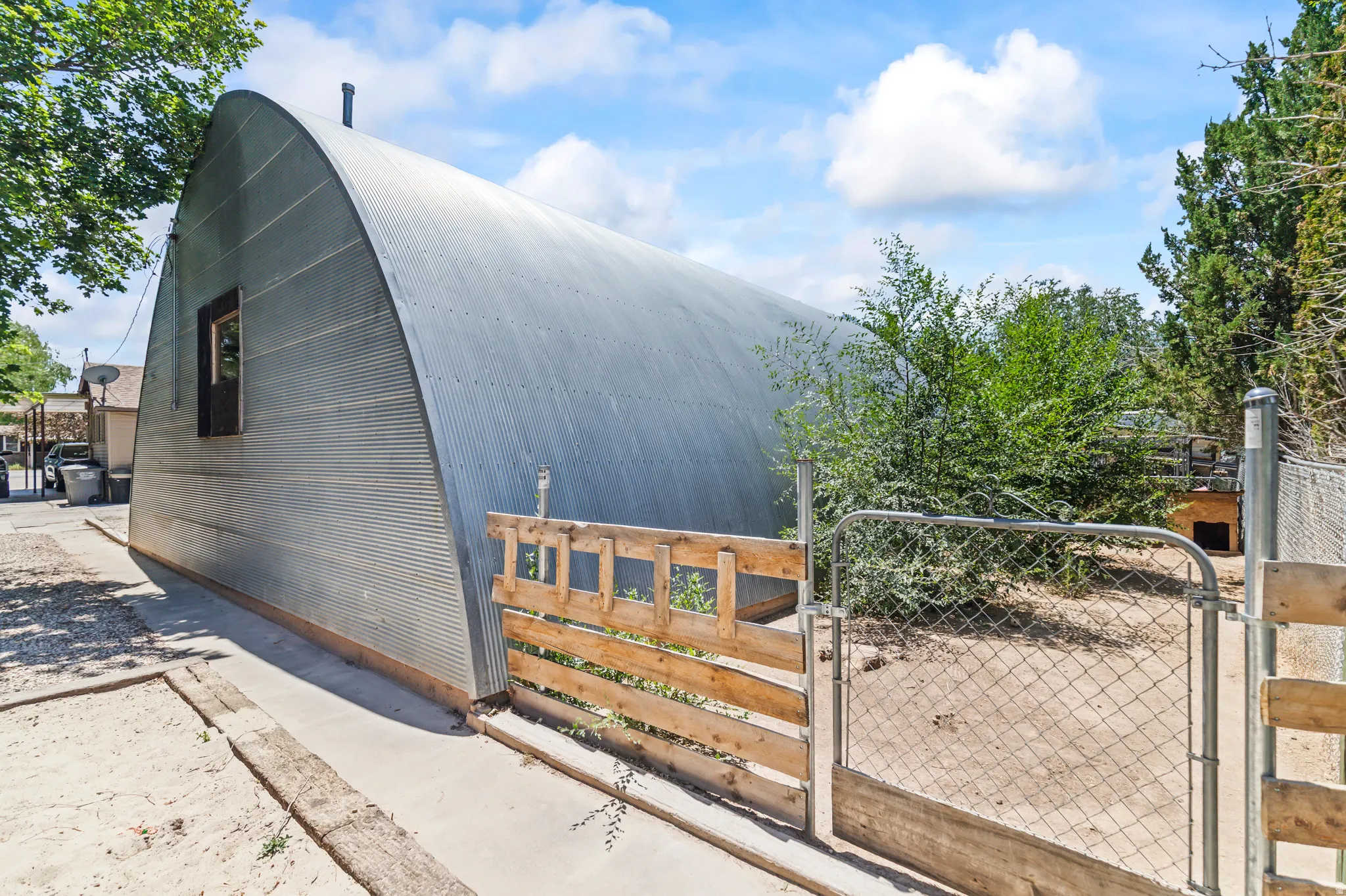 Corrugated metal quonset hut structure featuring a distinctive arched roofline, a single window with a dark trim, and a concrete perimeter