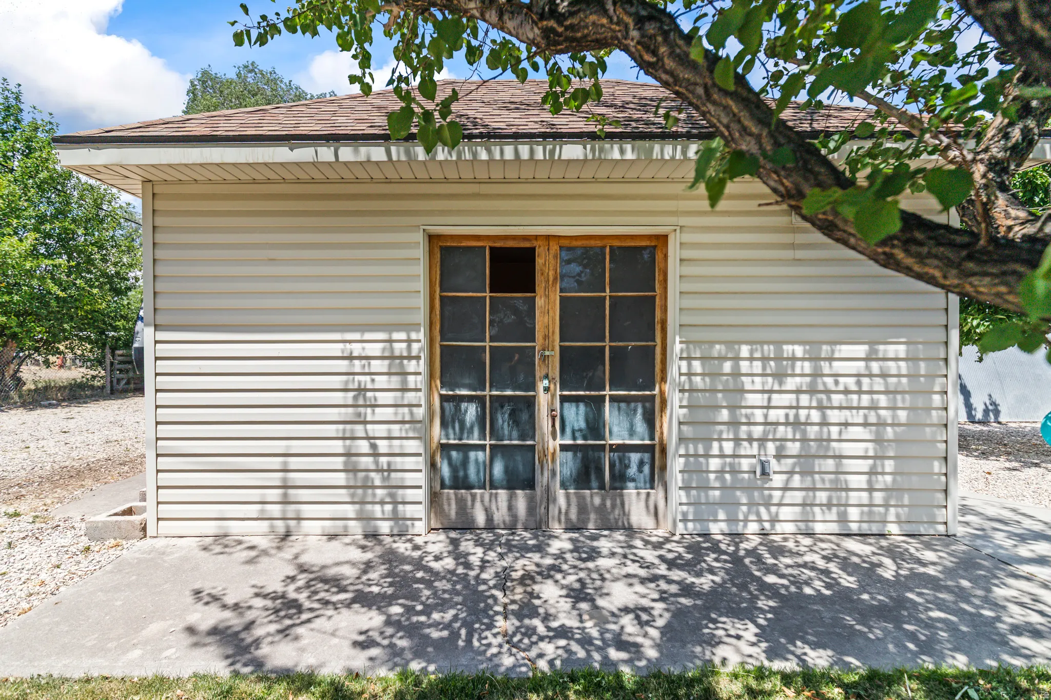 Exterior featuring light-toned horizontal siding, a brown shingled roof, and a concrete patio
