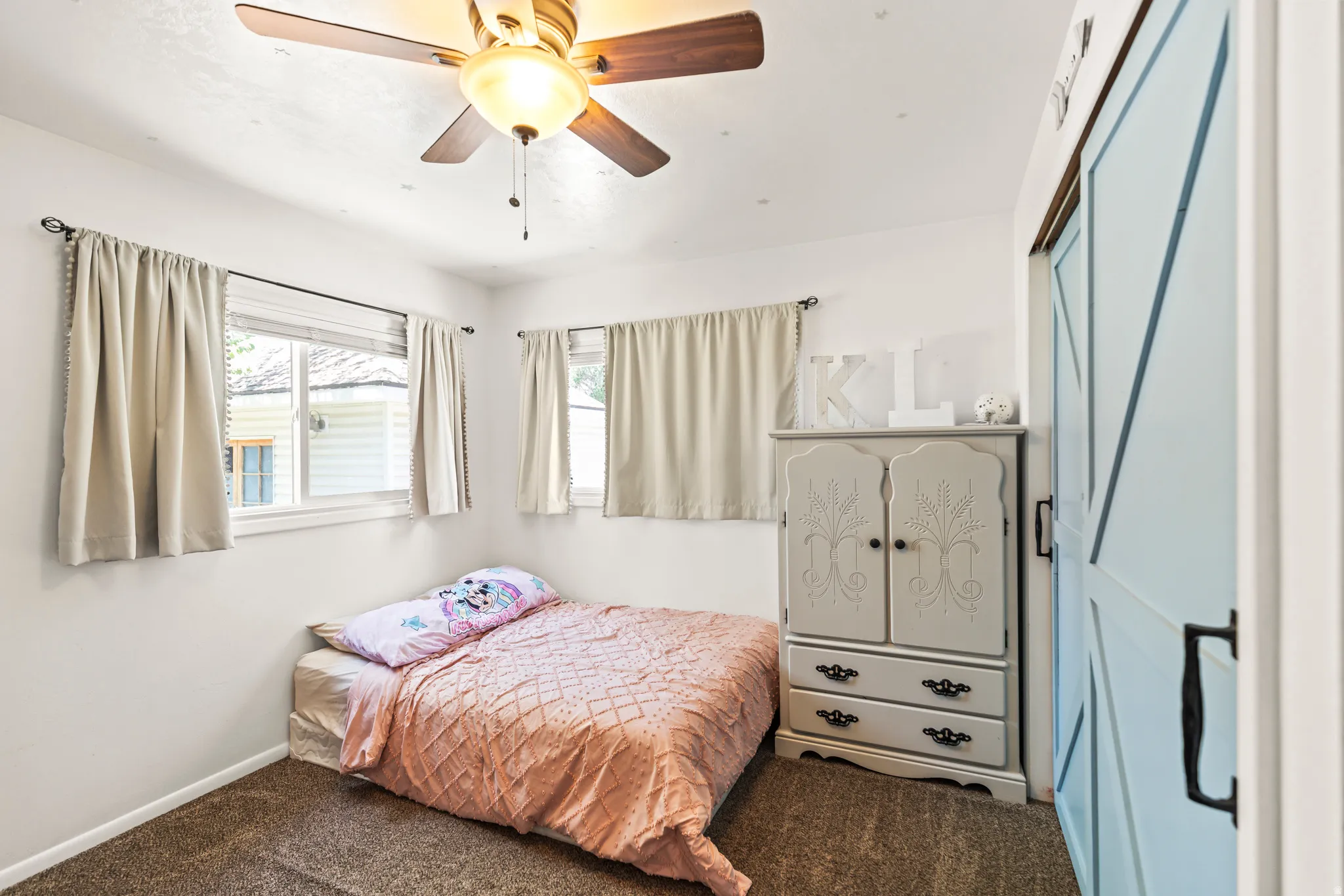 Interior room featuring a ceiling fan with light fixture, two windows with blinds, and light-colored carpeting