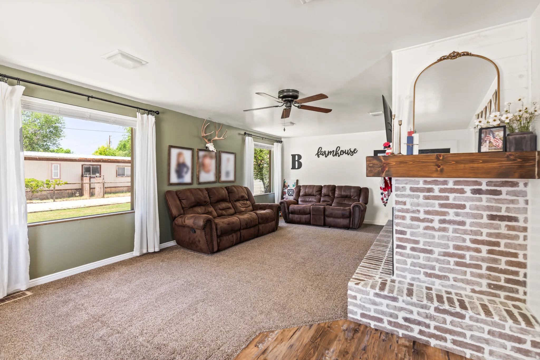 Spacious living area featuring a brick fireplace with a wood mantel, light-toned carpeting, and multiple windows