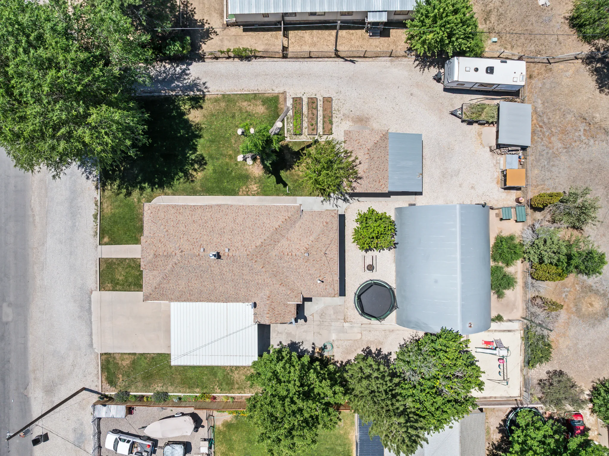 Aerial property overview featuring a main residence with a brown shingle roof, a detached metal-roofed structure, and a secondary covered parking area