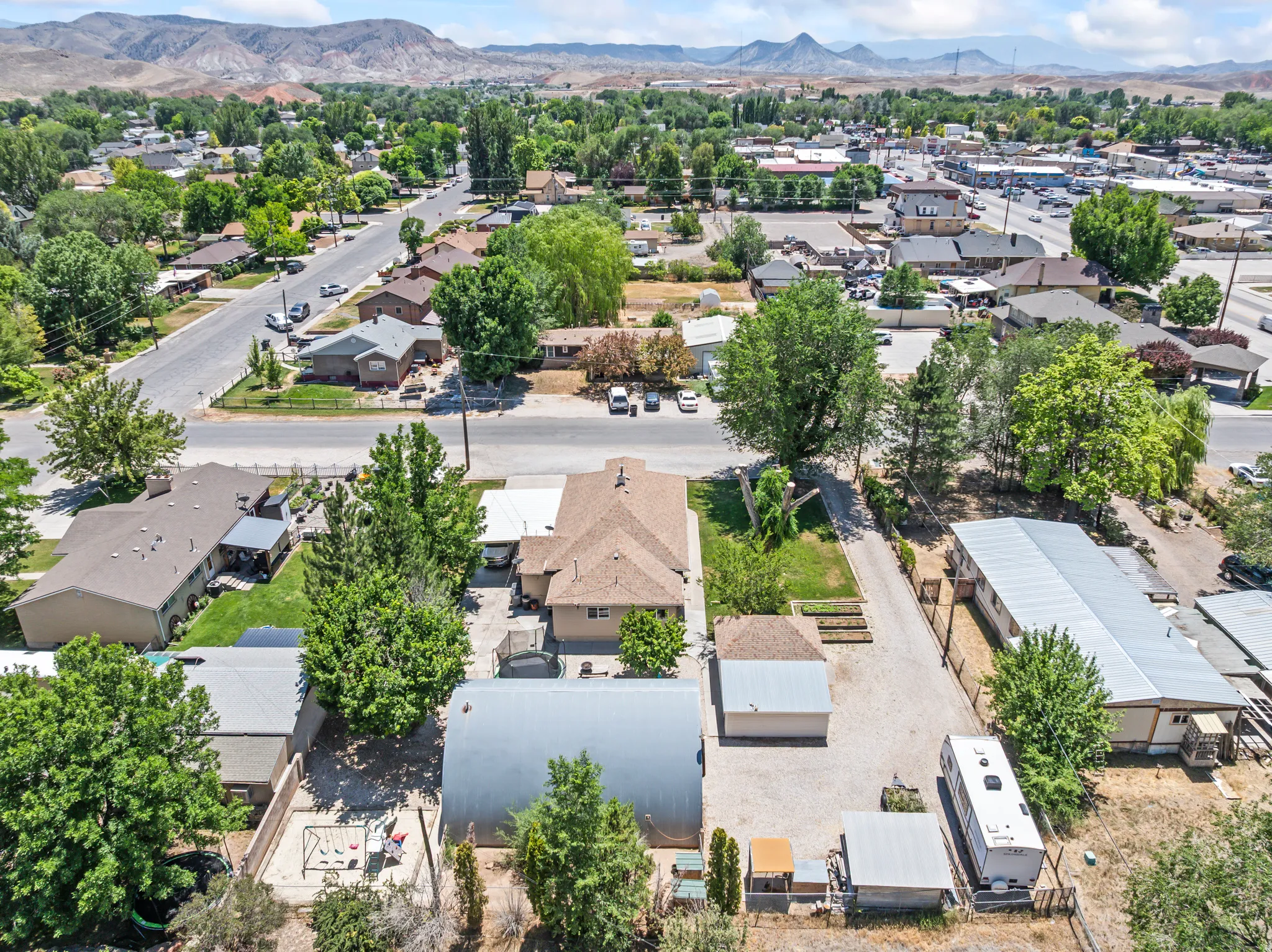 Expansive property featuring a gravel driveway, multiple outbuildings, mature trees, and a distant mountain backdrop