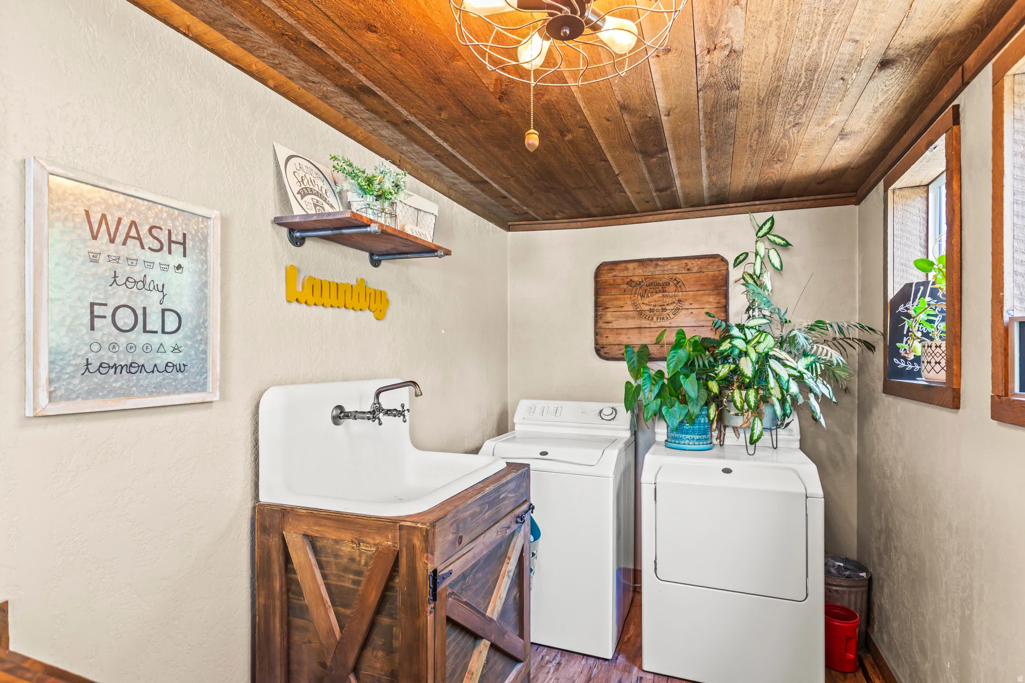 Laundry area featuring a wood-paneled ceiling, utility sink with a wood-finish cabinet, and two windows with wood trim