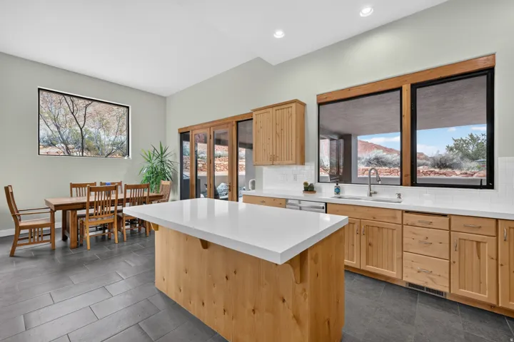Expansive kitchen island with a white countertop, natural wood cabinetry, white subway tile backsplash, recessed lighting, and large windows
