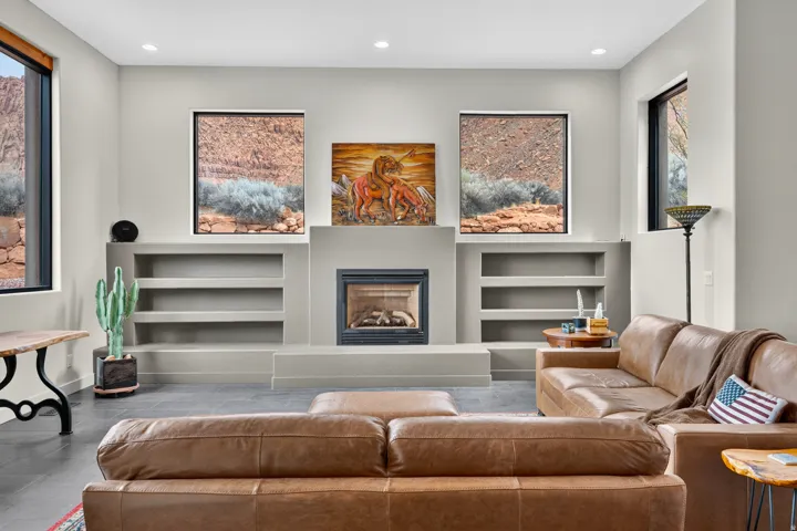 Integrated fireplace with a raised hearth, recessed built-in shelving, high ceilings with recessed lighting, and large windows