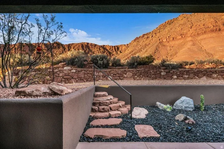 Desert landscaping featuring a stone retaining wall, natural rock steps, black pebble ground cover, and native plantings
