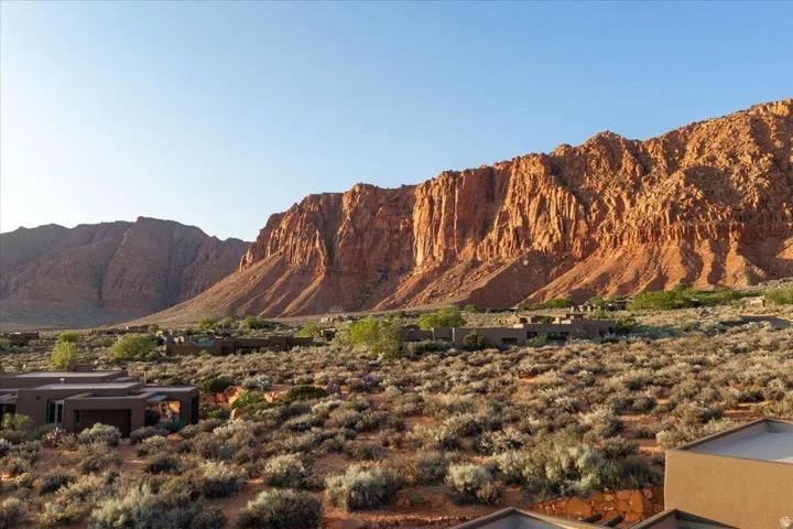 Dramatic red rock mountains frame the expansive desert landscape, featuring multiple low-profile, earth-toned structures integrated into the terrain