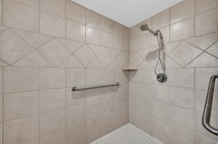Shower with neutral-toned square tile, diagonal accent band, built-in corner shelf, and brushed nickel shower head