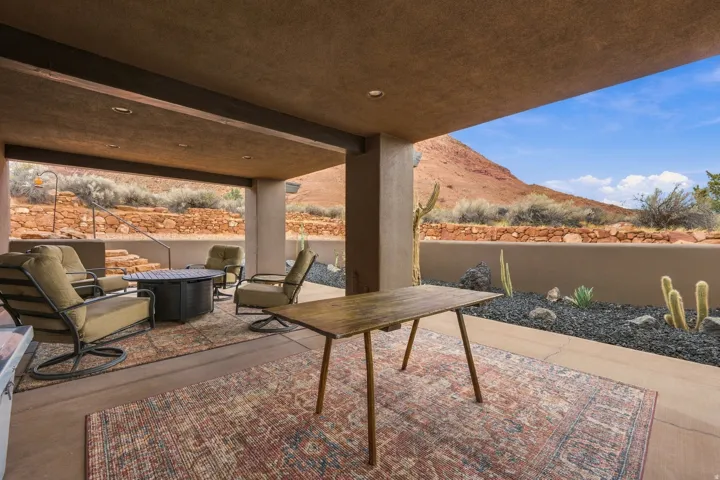 Covered patio space, recessed lighting, concrete patio surface, decorative rock landscaping, and a low retaining wall