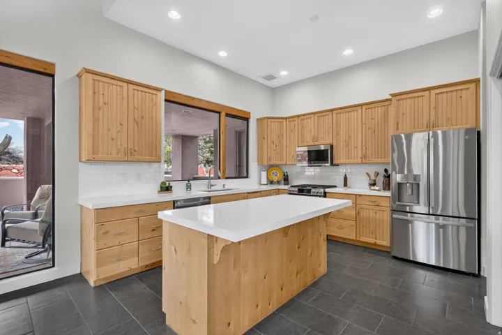 Wood-finish cabinetry, stainless steel appliances, white countertops, tile backsplash, and a central island