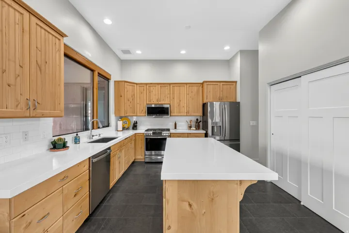 Kitchen featuring wood cabinetry, white countertops, stainless steel appliances, dark tile flooring, and a large window