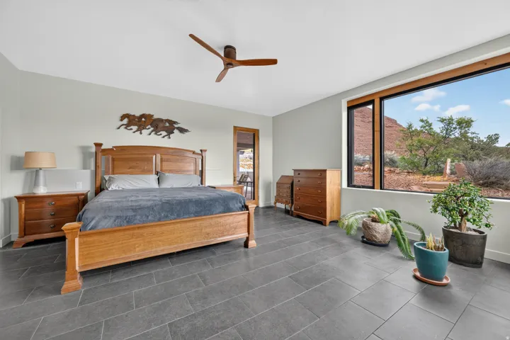 Spacious room featuring large format tile flooring, a wide window with a natural wood frame, and a ceiling fan with wood-finish blades