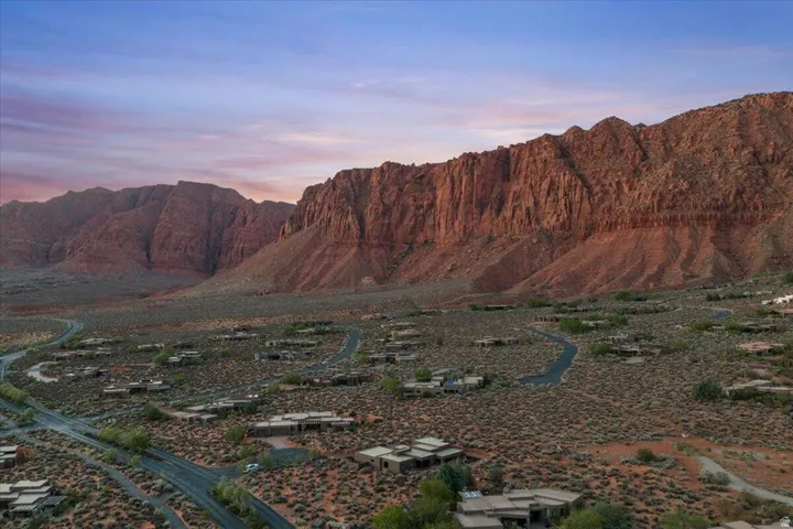 Expansive desert landscape featuring a residential community with contemporary low-profile homes, winding roadways, and mature desert vegetation set against dramatic red rock formations