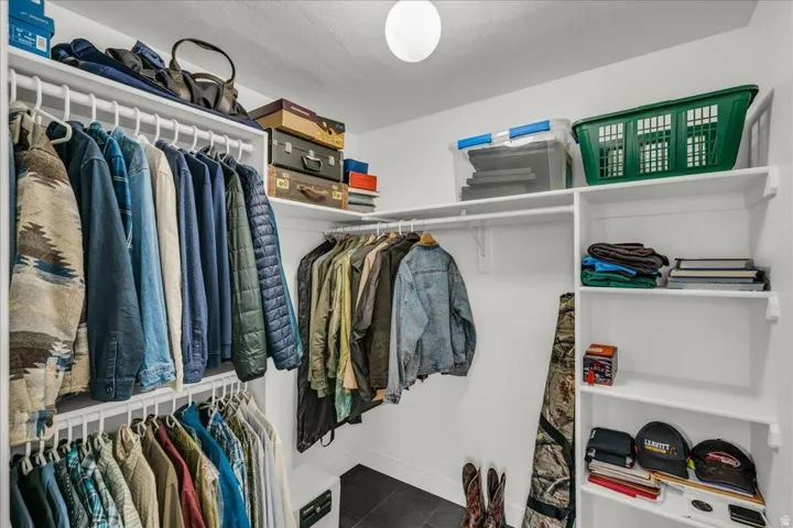 Spacious walk-in closet featuring white built-in shelving, multiple hanging rods, and dark tile flooring