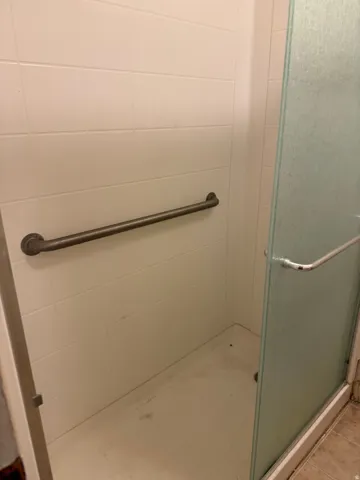 White tiled shower with a clear glass enclosure and a horizontal grab bar