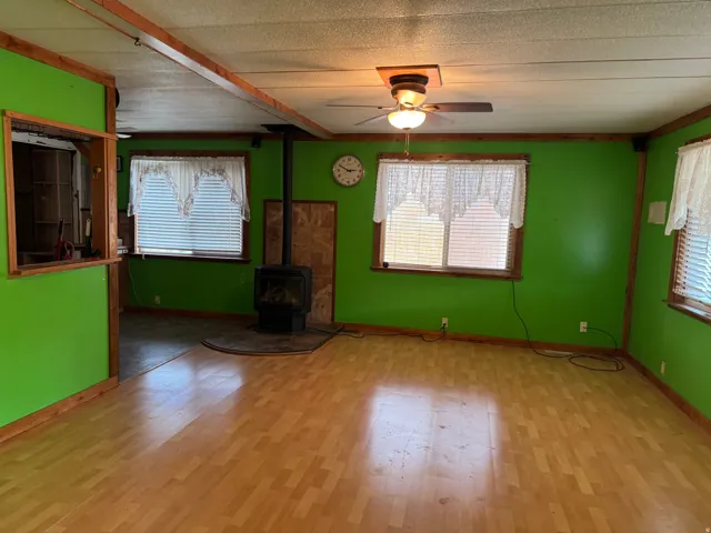 Living area featuring wood-finish flooring, a freestanding wood-burning stove with a tile surround, and multiple windows with blinds