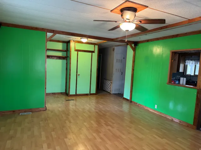 Spacious interior room featuring wood-finish flooring, vibrant green paneling, and an exposed wood beam ceiling