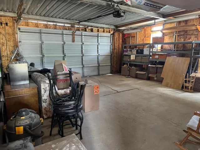 Attached garage with concrete flooring, overhead garage door, and exposed wood-paneled walls